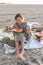 Little girl on the sandy seashore at a picnic with fruits.