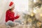 Little girl in Santa hat decorating window with snowflakes at home