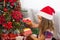 Little girl in Santa hat opens a red box with a gift and a Golden magic light near the Christmas tree. Holiday decor, poinsettias