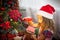 Little girl in Santa hat opens a red box with a gift and a Golden magic light near the Christmas tree. Holiday decor, poinsettias