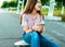 A little girl schoolgirl of 12-16 years old, on street she sits on a skateboard in summer in park. In hands of phone