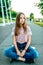 A little girl schoolgirl of 12-16 years old, on street sits skateboard in summer in park. Resting after walking and