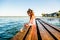 A little girl in shorts and a T-shirt sits on a pier by the lake in summer. Summer vacation