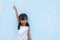 Little girl show arm and index finger pointed up on blue wall background.