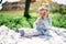 Little girl sits on a blanket on a green lawn and gnaws a bottle of water that she holds in her hands