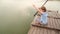 little girl sits with fishing rod caught small fish on bridge by river.