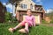 Little girl sits on grass near cottage and smiles