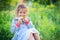 The little girl sits in a grass in the village and holds in hand of two chickens