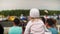 Little girl sits on parent`s shoulders in front of crowd and looks at car show