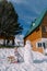 Little girl sits on a sleigh near a snowman in the courtyard of a wooden chalet