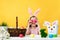 A little girl sits at a table and holds Easter eggs in her hands. Happy child in bunny ears on a background of yellow wall