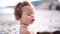 Little girl sits thinking on the beach, and her mother straightens her dress