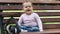 Little girl sits on a wooden bench in a city park