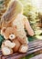 little girl sitting back with teddy bear on the bench in sun beams outside in the park