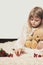 Little girl sitting on the carpet, with her teddy bear, playing with Christmas decoration