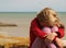 Little girl is sitting clasping her knees and bowing her head by the sea