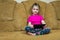 Little girl sitting on a comfortable couch enjoying an online game on a digital tablet computer. Addicted to technology