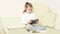 A little girl is sitting on the couch in the living room and holding a tablet in her hands. in the interior