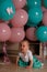 Little girl sitting on the floor in the room next to the balloons, first birthday, celebrate. one year old blue and pink balls wit