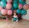 Little girl sitting on the floor in the room next to the balloons, first birthday, celebrate. one year old blue and pink balls wit