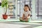 Little girl sitting in lotus pose with hands in ahamkara mudra. Child performing meditation at home on a beautiful sunny day