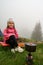 A little girl is sitting near a burner on which dinner is being prepared, resting with a tent.