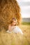 Little girl sitting near stack of hay summer
