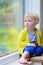 Little girl sitting next window on rainy day