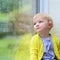 Little girl sitting next window on rainy day