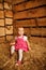 Little girl is sitting on pile of straw in hayloft