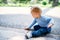 Little girl sitting on the road in the park and scratching tiles with her finger