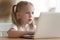 Little girl sitting at table watching cartoons on laptop