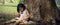 Little girl sitting under a big tree and writing a book.