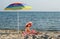 Little girl sitting under sunshade on beach