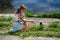 A little girl is sitting by the water and reaches out to a small crow