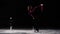 A little girl skater in a black sports suit and white skates performs a spinning stand in the arena of the ice stadium