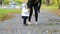 Little girl in skirt and mother walk in autumn park