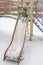 A little girl slides down a slide on a playground in winter.