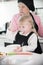 A little girl sloppy eating a sour cream while her grandmother making pancakes