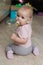 Little Girl with soother. little baby with a pacifier. in a pink sweater and gray pants sits on the floor