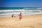 Little Girl in Spotty Runs to Wave Surf Boy Plays on Beach