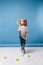 Little girl standing with tennis raquet and balls on blue