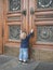 A little girl standing on tiptoe stretches her hands to the massive doors of the university trying to open them