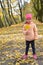 Little girl stands on autumn park alley with maple leaf in her hand