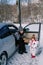 Little girl stands near her mother sitting in a car with an open door with a lunchbox in her hands