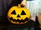 A little girl stands next to Jack`s orange pumpkin on a dark background. The baby touches the pumpkin with her finger. A pumpkin w