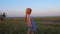 Little girl in a straw hat, blue plaid summer dress in grass field countryside on sunset. Child with long blonde braid.