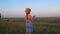 Little girl in a straw hat, blue plaid summer dress in grass field countryside on sunset. Child with long blonde braid.