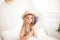 Little girl in a straw hat and dress on a background of a bright white bedroom with a rustic interior. Childhood concept. Provence