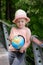 A little girl in a straw hat is holding a globe in her hands. Child considers the model of the globe.
